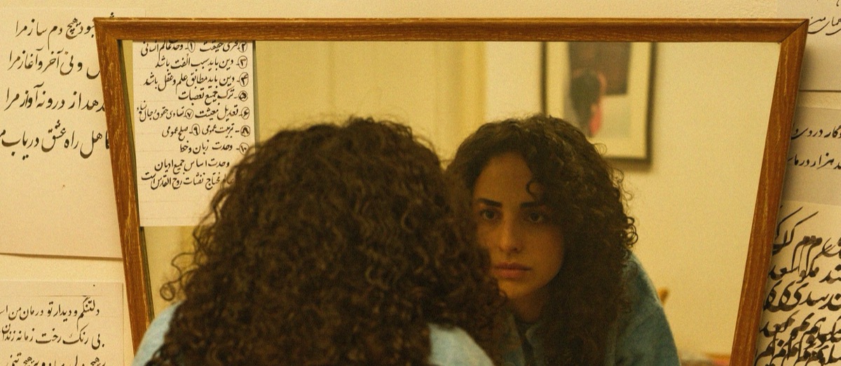 Parmiss Sehat as Layla in Cast Aside the Clouds — reflected in a mirror, Persian script covering the walls around her.